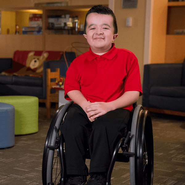 Shriners patient Alec smiling in wheelchair in hospital playroom