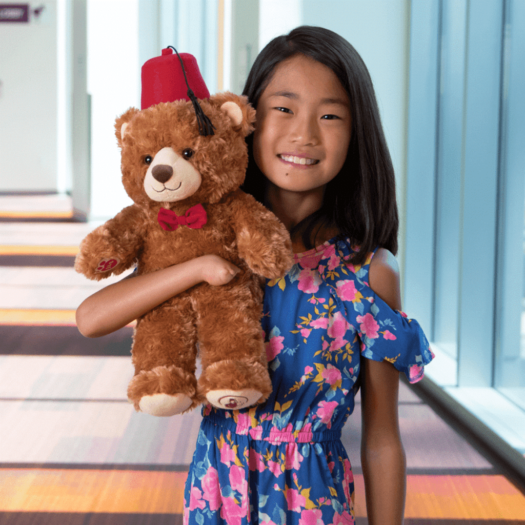 Girl Shriners patient holds Fezzy the bear