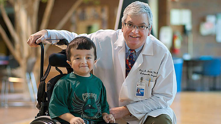 Shriners doctor smiles alongside patient Alec in hospital