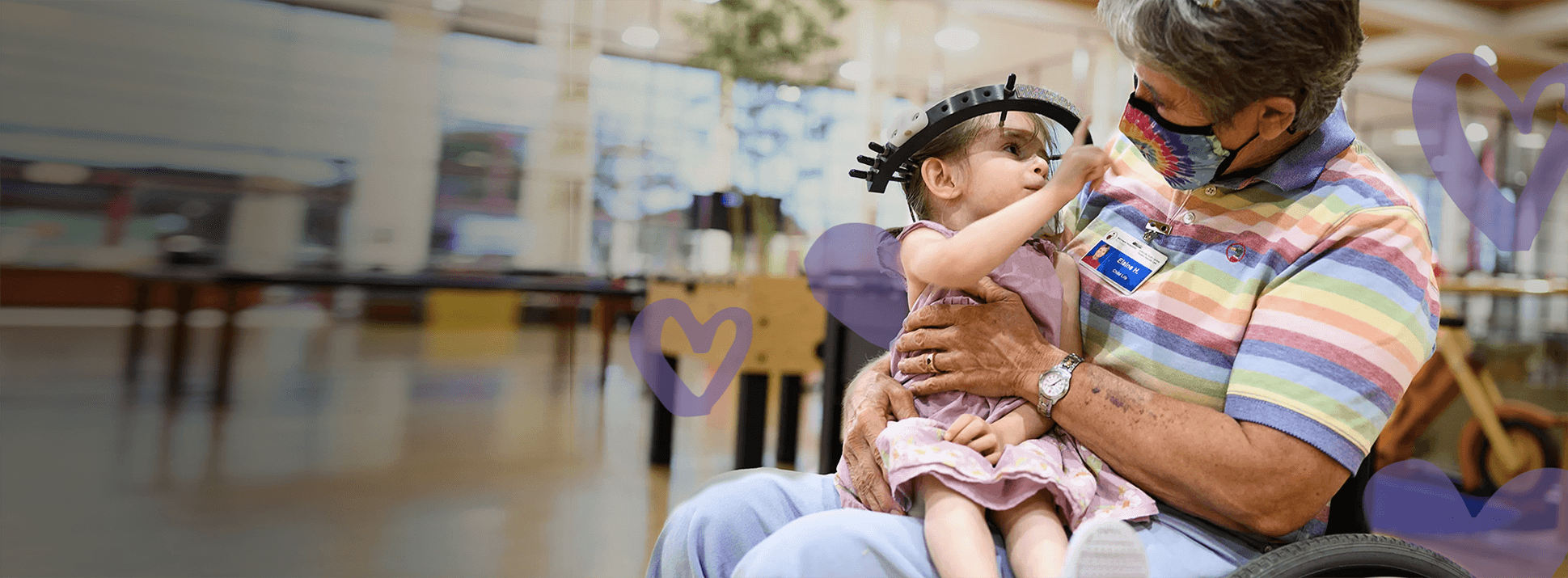 Young female shriners patient with halo medical device sits in female nurses lap