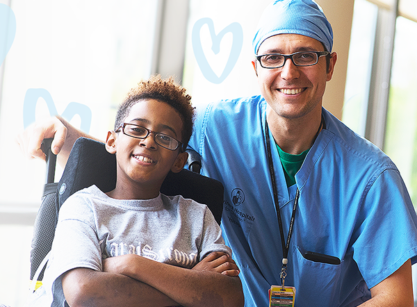Shriners doctor in scrubs smiles alongside young male patient