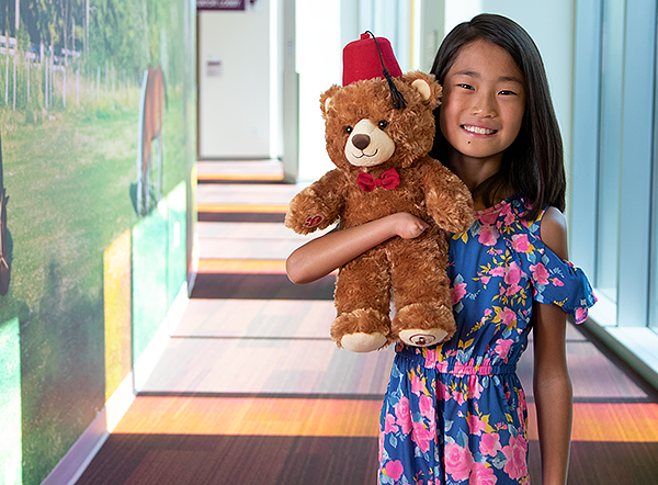 Girl Shriners patient holds Fezzy the bear