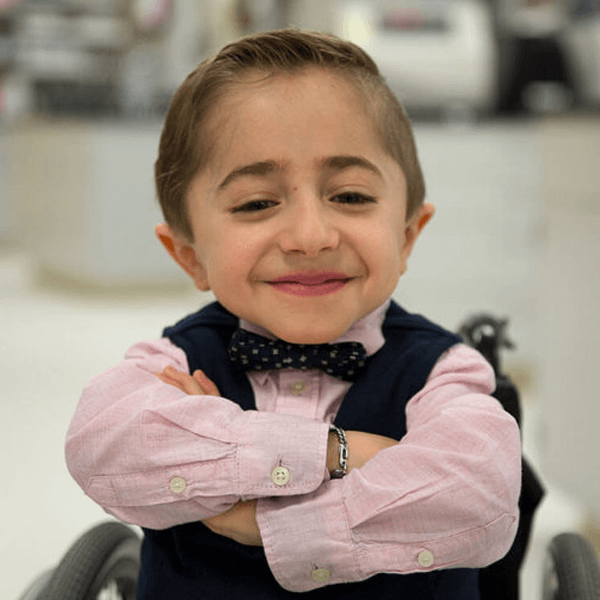 Shriners patient Kaleb smiles with arms crossed in wheelchair
