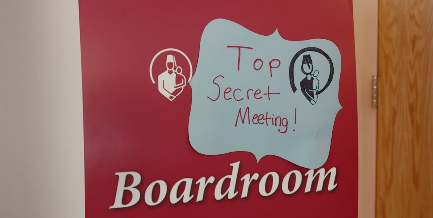 A photo of the Shriners boardroom door with a sign that says "Top Secret Meeting" on it.